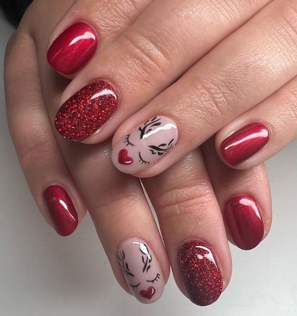 A closeup of a woman's fingernails with a combination of nude and red nail polish that has deep red glitter and reindeer nail art
