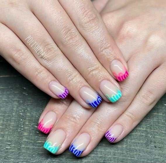 A woman's fingernails with a glossy nude nail polish that has multicolored French tips