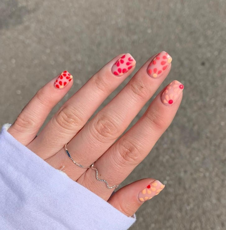 A woman's fingernails with nude nail polish base that has red daisies nail art