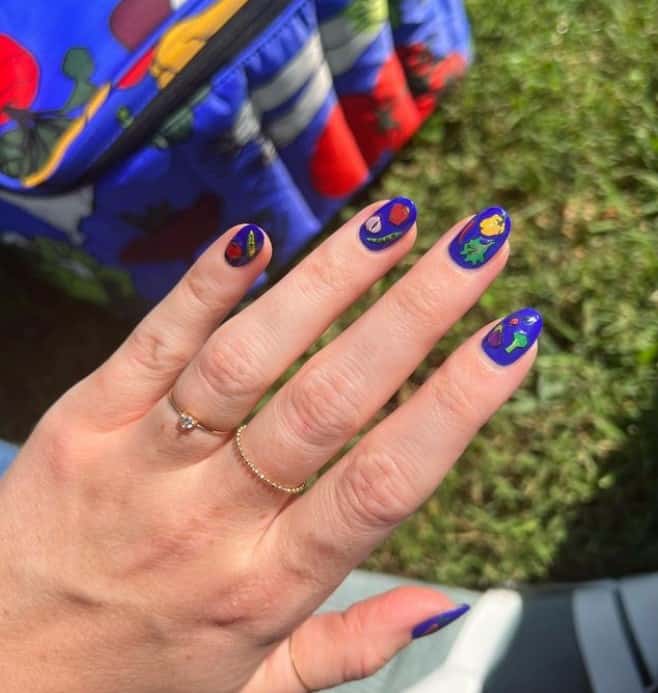 A closeup of a woman's fingernails with bold blue nail polish that has veggie nail art 