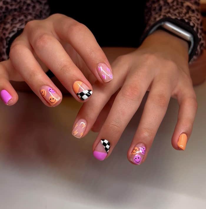 A woman's fingernails with a nude nail polish base that has black and white checkers, smiley faces and lightning bolts 