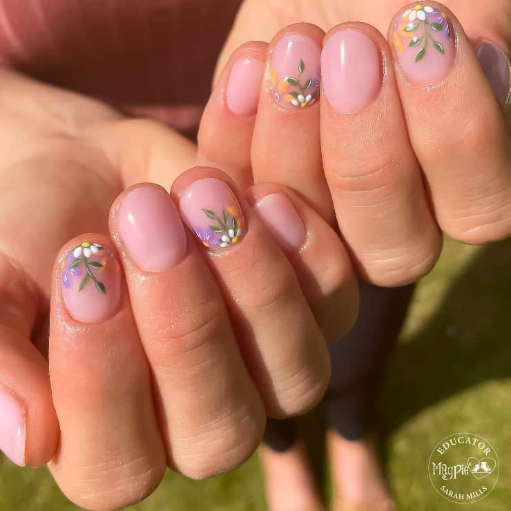 A closeup of a woman's fingernails with a pale pink nail polish that has floral nail art on select nails 
