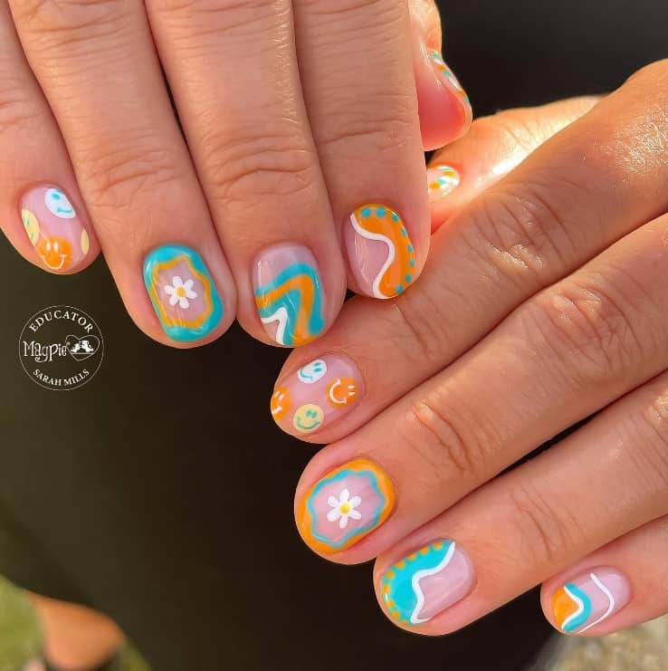 A closeup of a woman's fingernails with a beautiful nude nail polish base that has turquoise and orange abstract nail designs and smiley faces and daisies