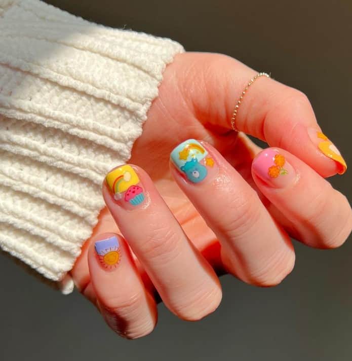 A closeup of a woman's fingernails with a ɴuᴅᴇ nail polish base that has Care Bear, cupcakes, flowers, rainbows, and stars nail designs