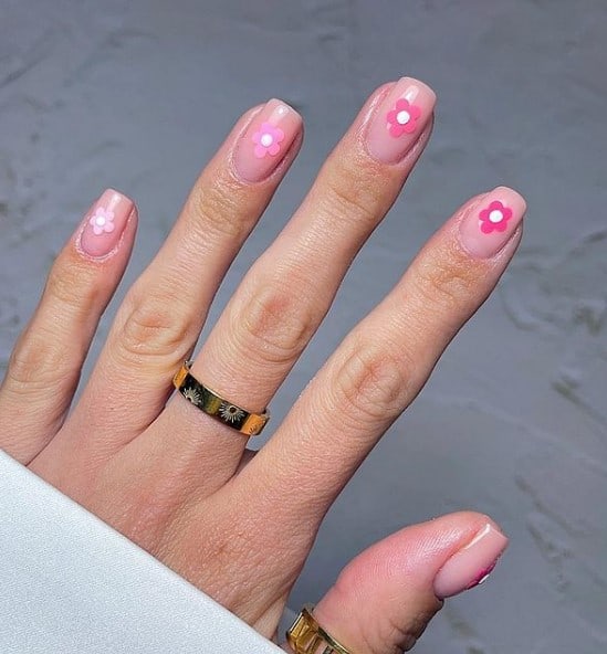 A woman's fingernails with pale pink nail polish that has pretty pink flowers on each nails 