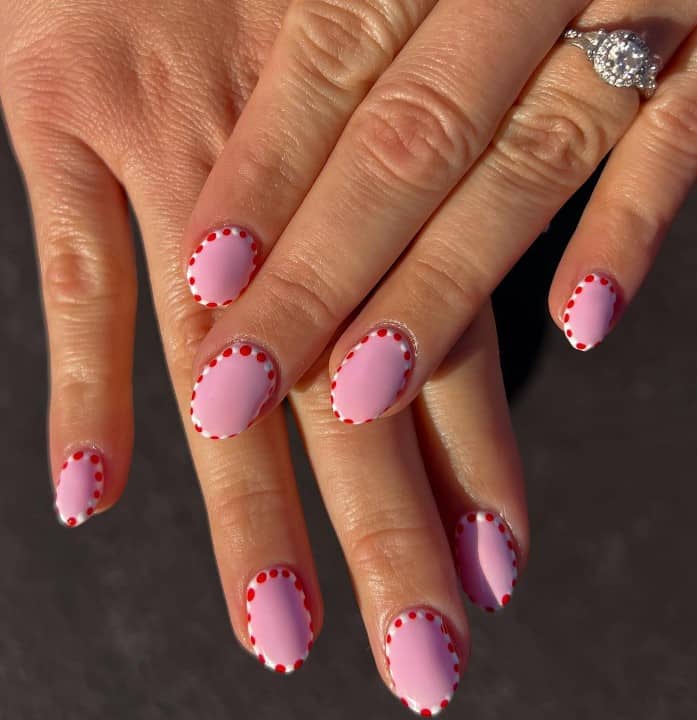 A woman's fingernails with a pale pink nail polish that has red-and-white peppermint outline