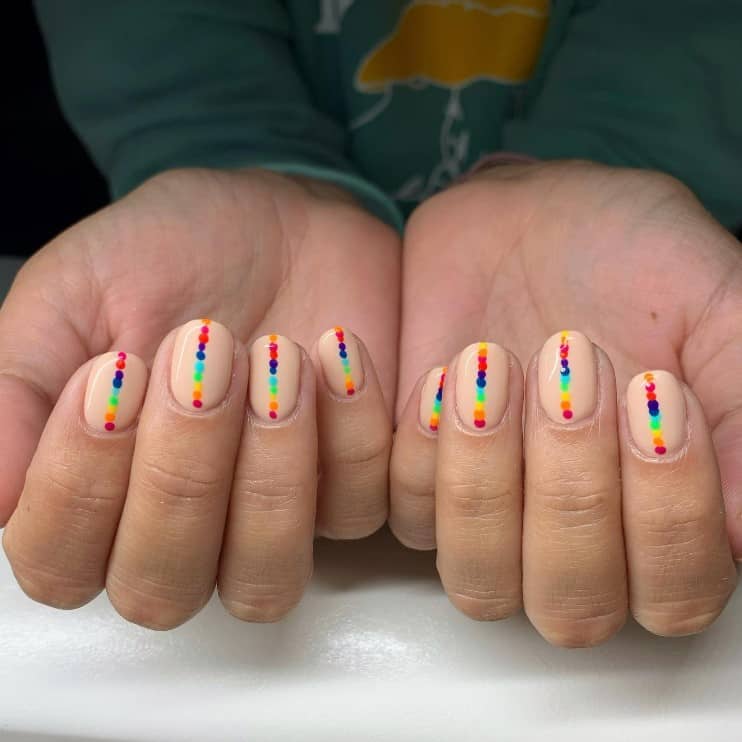 A closeup of a woman's fingernails with a nude nail polish that has rainbow-dot nail art 