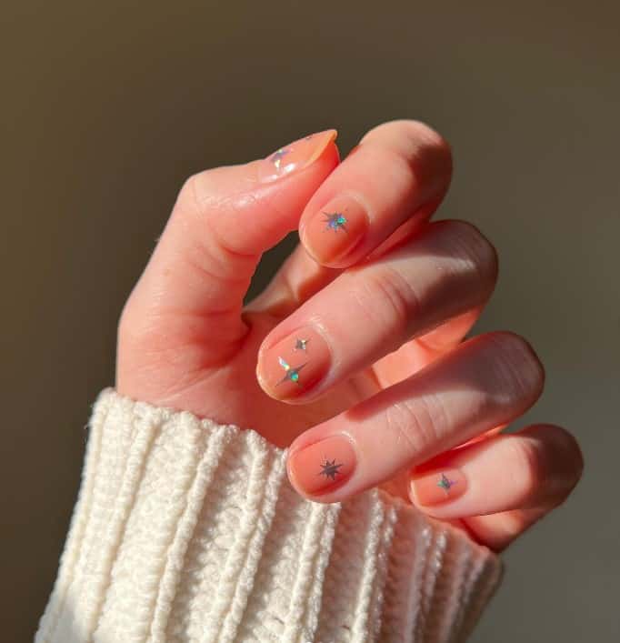 A woman's fingernails with a peach nail polish that has silver star stickers on each nail