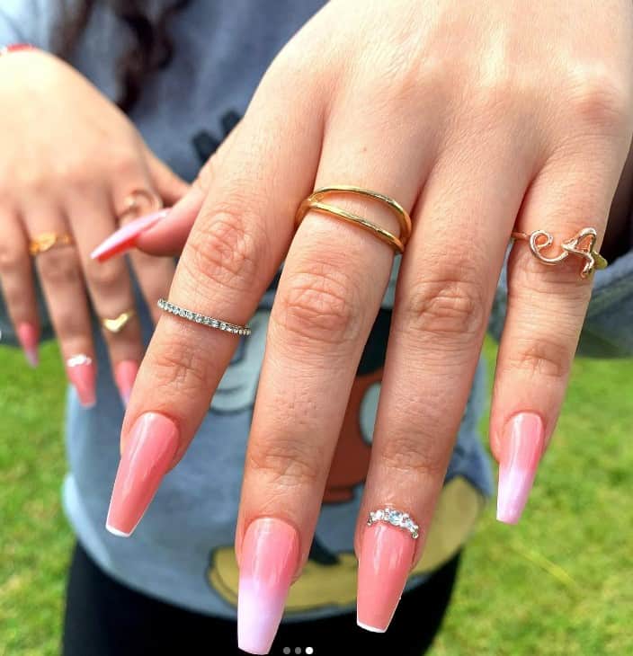A woman's fingernails with a soft pink nail polish base that has faded white tips and sparkling diamonds