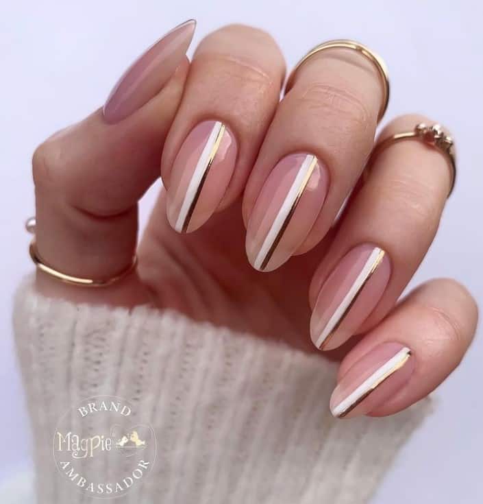 A closeup of a woman's fingernails with a soft nude pink base color that has a striking white and gold sideline 