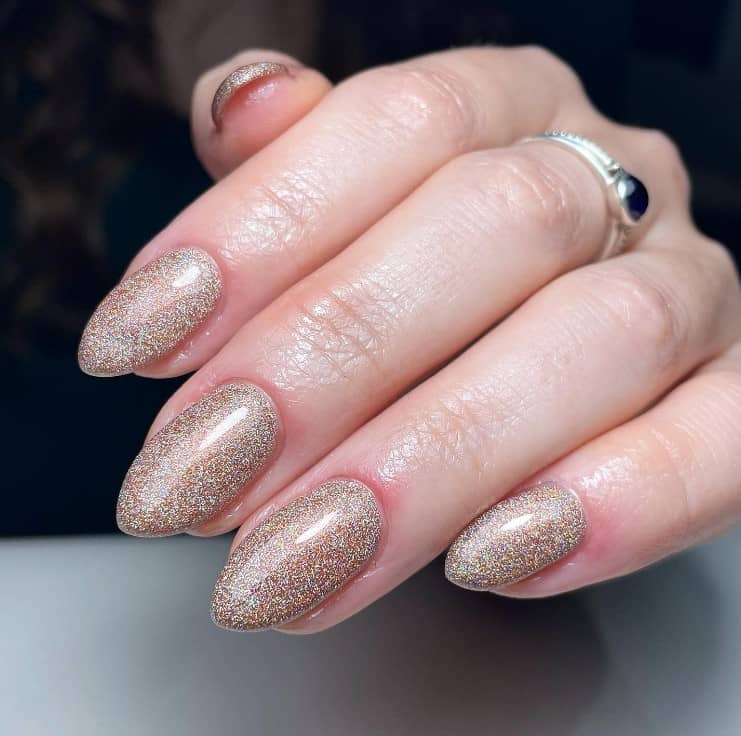 A closeup of a woman's fingernails with a glossy top coat that has gold and silver glitter