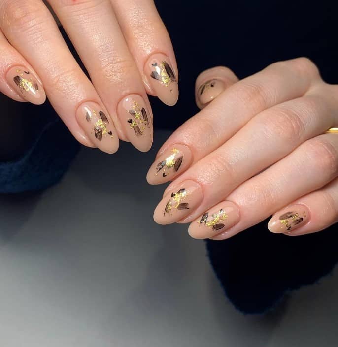 A closeup of a woman's fingernails with a nude nail polish base that has gold foil and hand-painted hearts