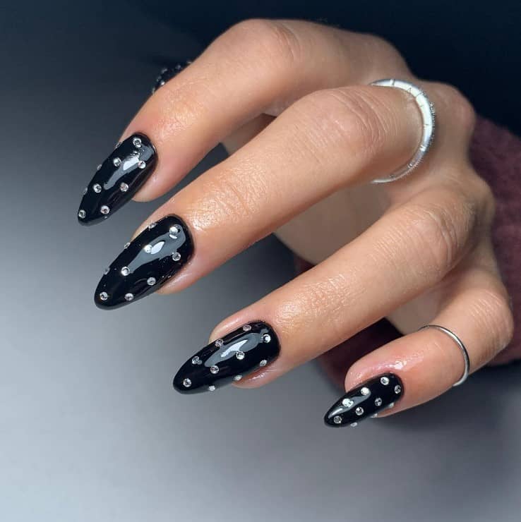 A closeup of a woman's fingernails with black nail polish that has rhinestones nail designs