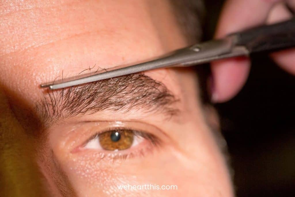 A closeup of a man's eye cutting his eyebrow hairs