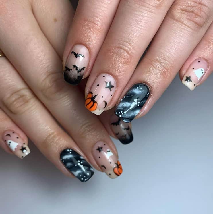 A closeup of a woman's fingernails with a peach and black nail polish that has pumpkins, bats, ghosts, and stars, while a striking black-and-white marble nail designs