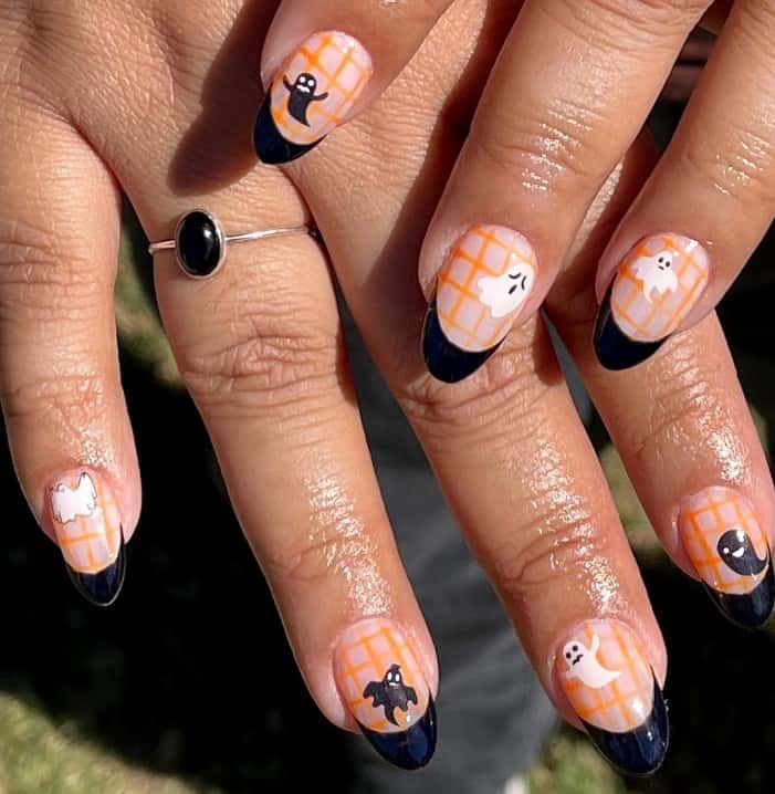 A closeup of a woman's fingernails with orange plaid patterns and glossy black tips that has cute ghost nail art in black and white
