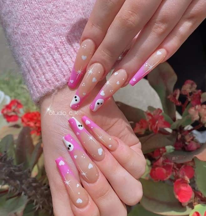 A closeup of a woman's fingernails with a peach nail base that has pink tips, white ghosts, sparkles, and hearts to each nail