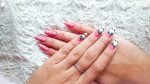 A woman's fingernails with a pink nail polish base that has skull tips and eyeballs nail designs