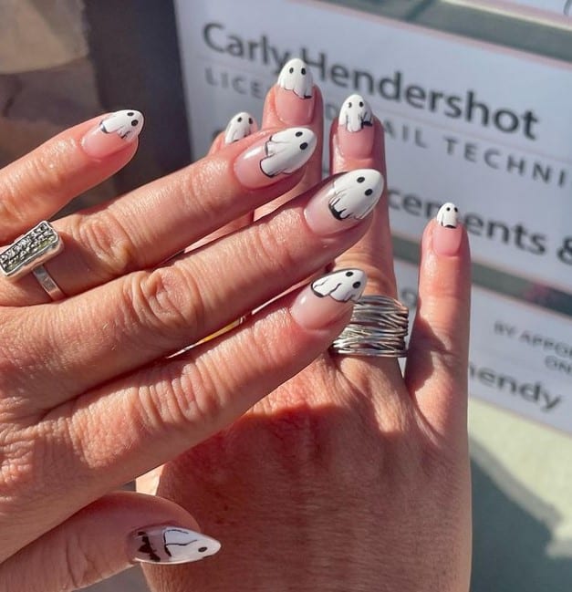 A closeup of a woman's chic and spooky fingernails with clear base that has terrifying white ghosts with black details