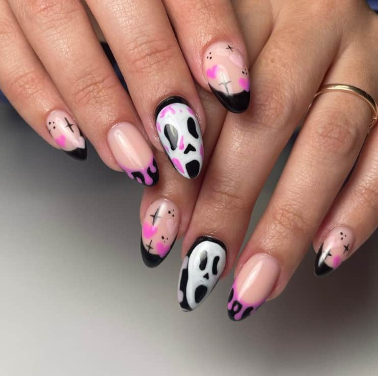 A closeup of a woman's fingernails with bewitching combination of black, white, pink, and violet hues that has various designs, including pinkish-purple drippings, screaming white ghosts, and cutesy hearts, stars, and dots