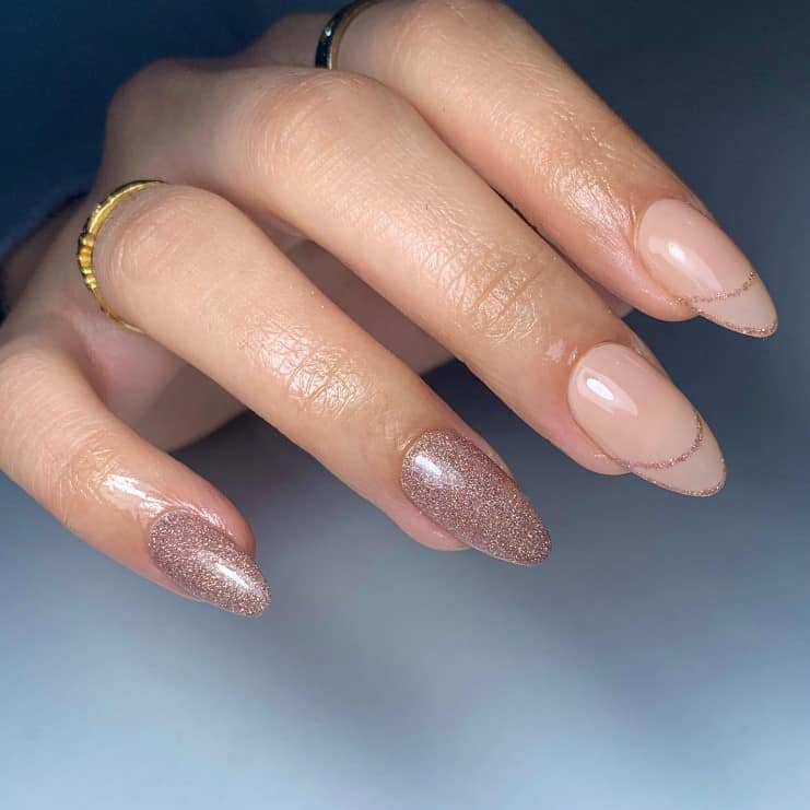 A closeup of a woman's fingernails with a combination of brownish-nude nails that has a gold glitter finish and rose gold glitter polish