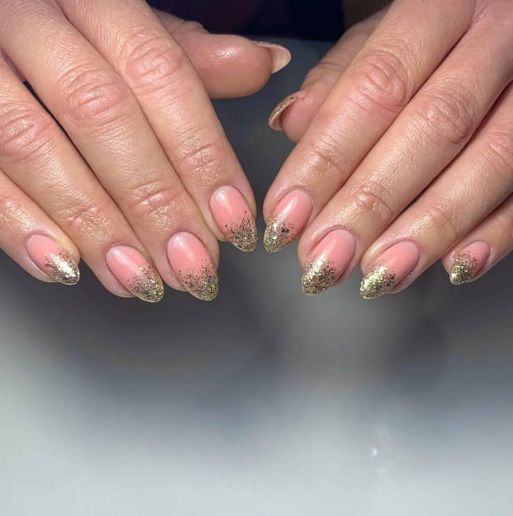 A closeup of a woman's fingernails with a pink nail polish base that has ombré French tips in gold glitter