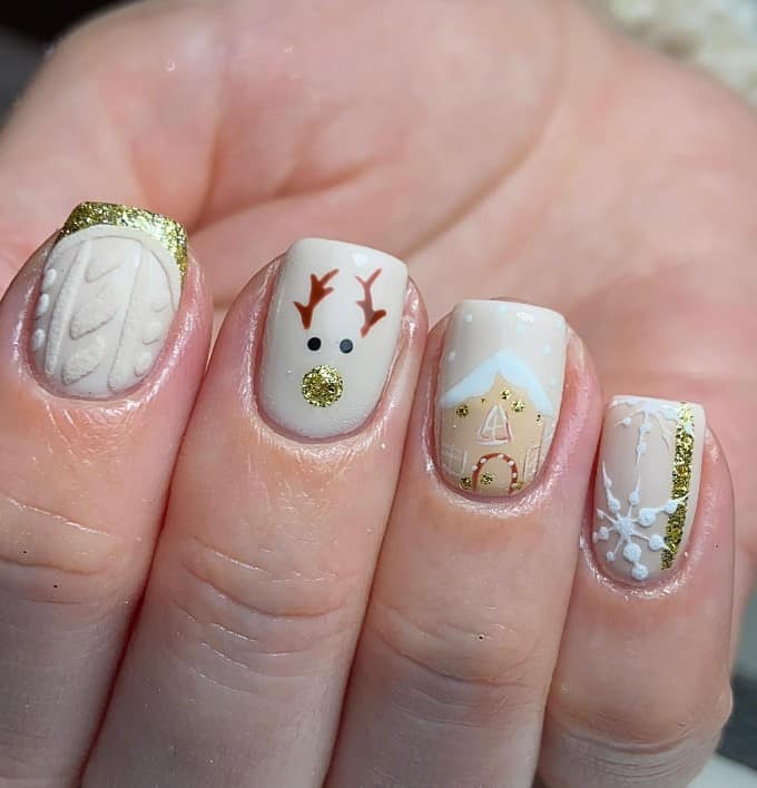 A closeup of a woman's fingernails with a white nail polish base that has white sweater, gold French tips, snowflakes, gingerbread houses, and reindeer nail designs