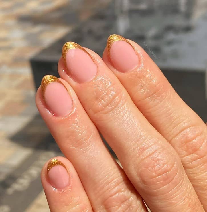 A closeup of a woman's fingernails with a clear nail base that has deep gold glitter French tips 