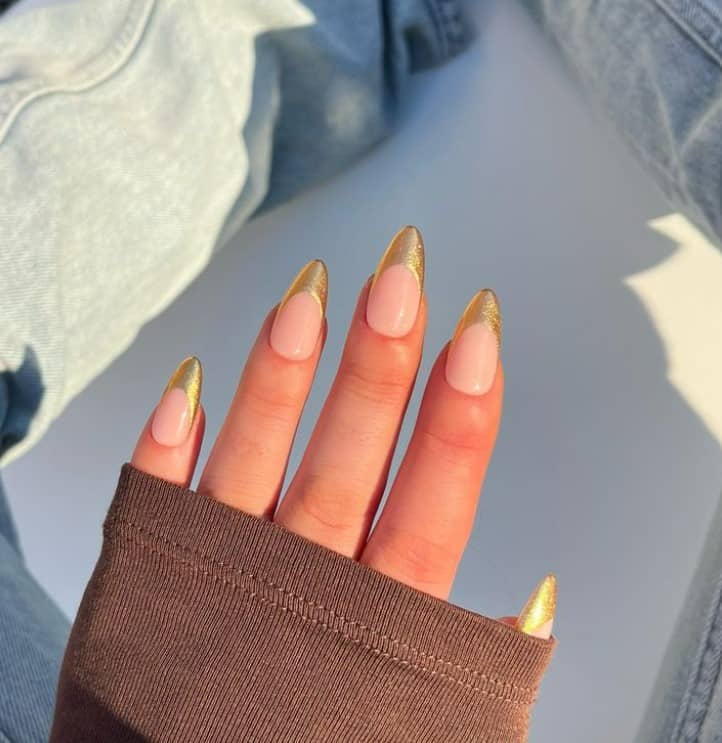 A woman's fingernails with a peach colored nails that has gold French tips