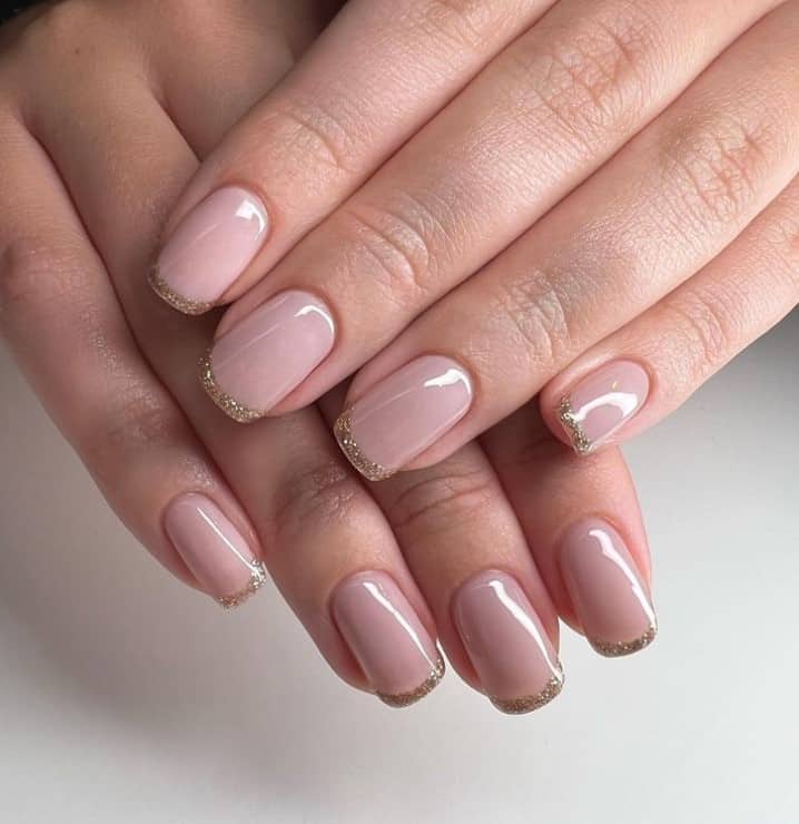 A closeup of a woman's fingernails with a soft pink base that has gold French tips