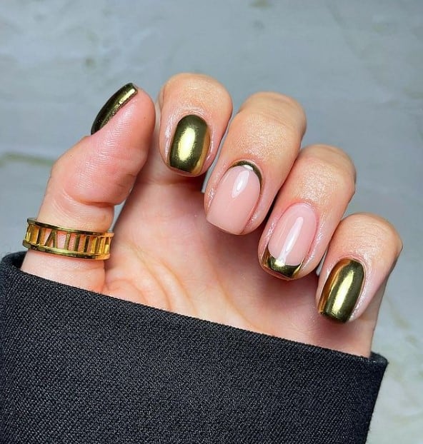 A woman's fingernails with a combination of nude and gold nail polish base that has subtle gold French tip on the ring finger and a gold cuticle cuff on the middle finger