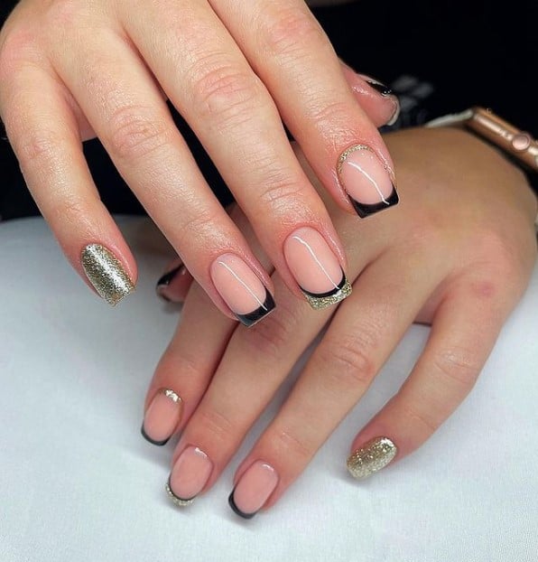 A woman's fingernails with a a combination of nude and gold glitter nail polish that has gold French tips with a black outline, black French tips with gold cuticle cuffs, and simple black French tips