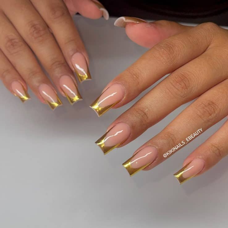 A woman's fingernails with a glossy nude nail polish base that has gold chrome French tips