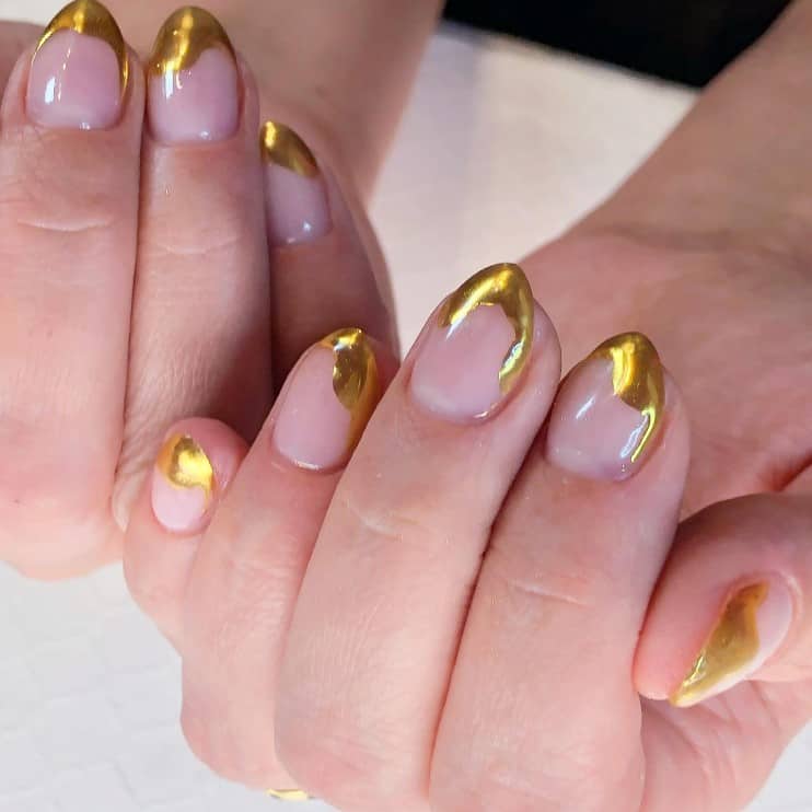 A closeup of a woman's fingernails with a clear nail base that has dripping liquid gold French tips