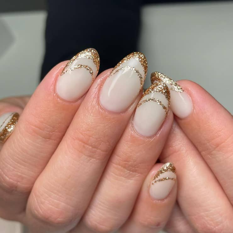 A closeup of a woman's fingernails with a white nail polish base that has double French tips in gold glitter