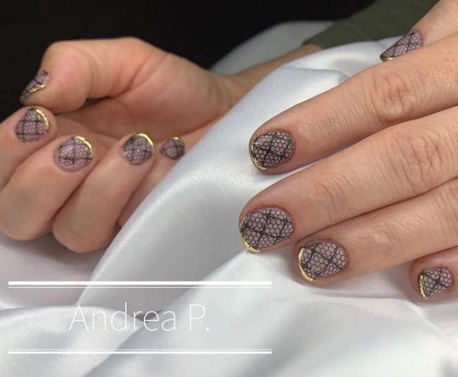 A woman's short round fingernails with lace-inspired look in black complete that has thin gold French tips