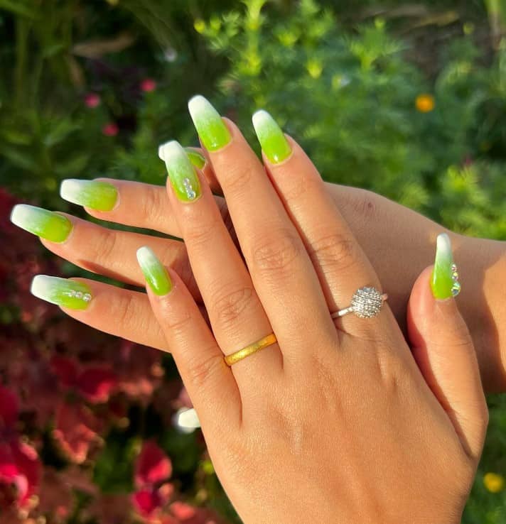 A woman's fingernails with a bright lime green hue that has white at the tips with silver jewels on select nails 