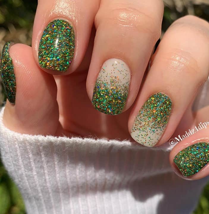 A closeup of a woman's fingernails with green-glitter-and-white-chrome ombré effect that has dazzling green glitter nails