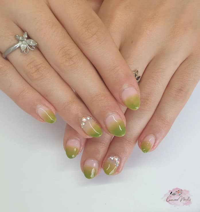 A closeup of a woman's fingernails with a pear-green-and-nude ombré effect polish that has rhinestones on select nails