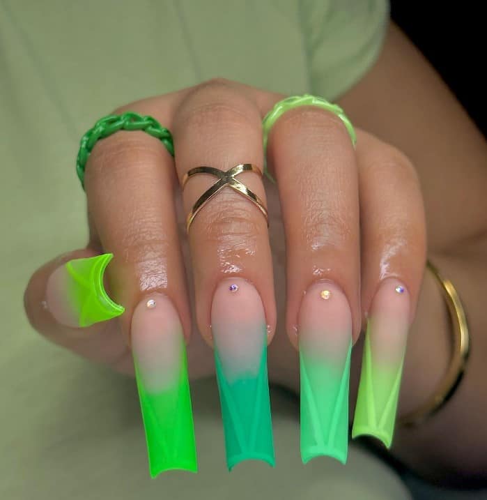 A closeup of a woman's fingernails with a nude nail polish base that has different shades of green with tiny gems, geometric lines, and a unique green hue to each nail