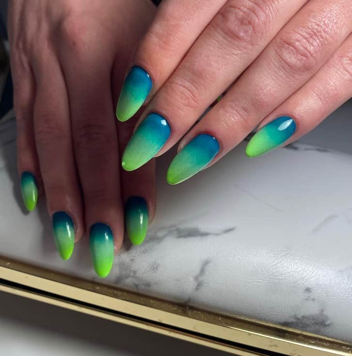 A closeup of a woman's fingernails with ombré effect that transitions from a deep blue to a serene green nail polish 