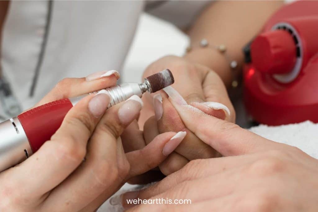 A closeup of a manicurist's hand sanding the polygel nails with an electric buffer in a salon