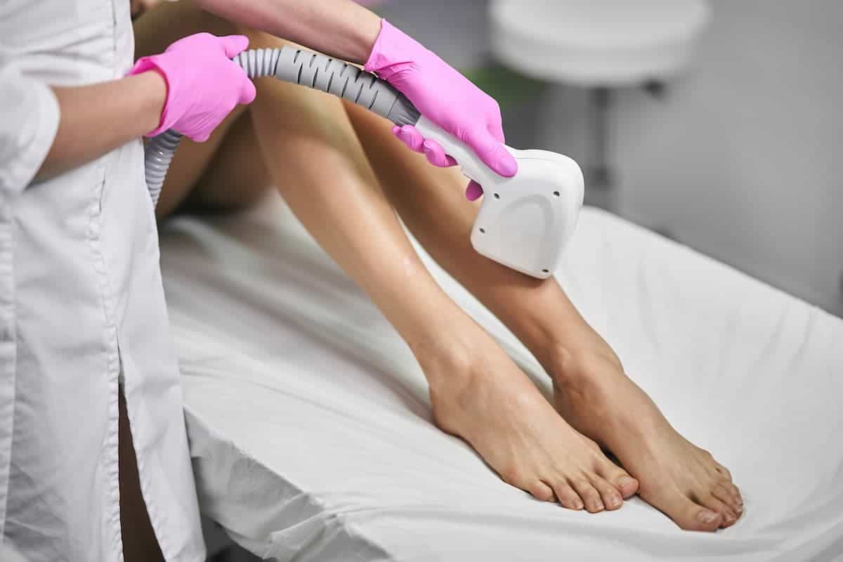 A cosmetologist is using a laser hair removal treatment on a woman's legs in a beauty salon