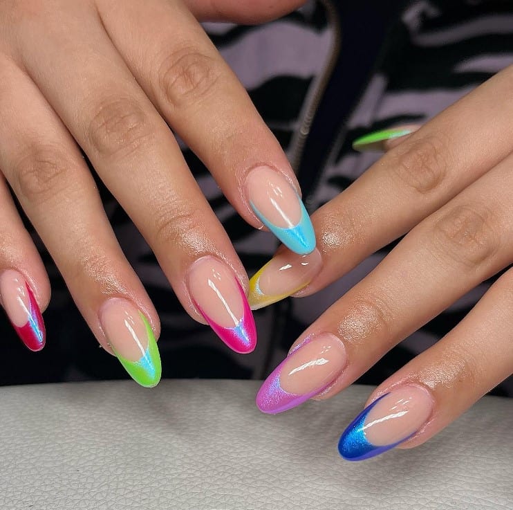 A closeup of a woman's fingernails with nude nail polish base that has glittery tips in different colors