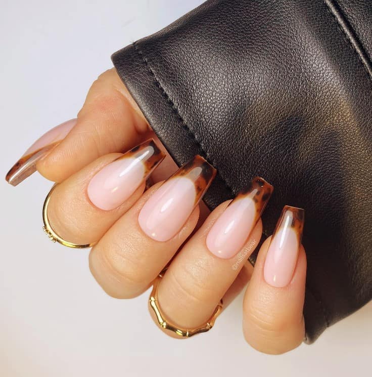 A woman's fingernails with a glossy pale pink nail polish that has Brown and black hues that looks like a tortoiseshell designs