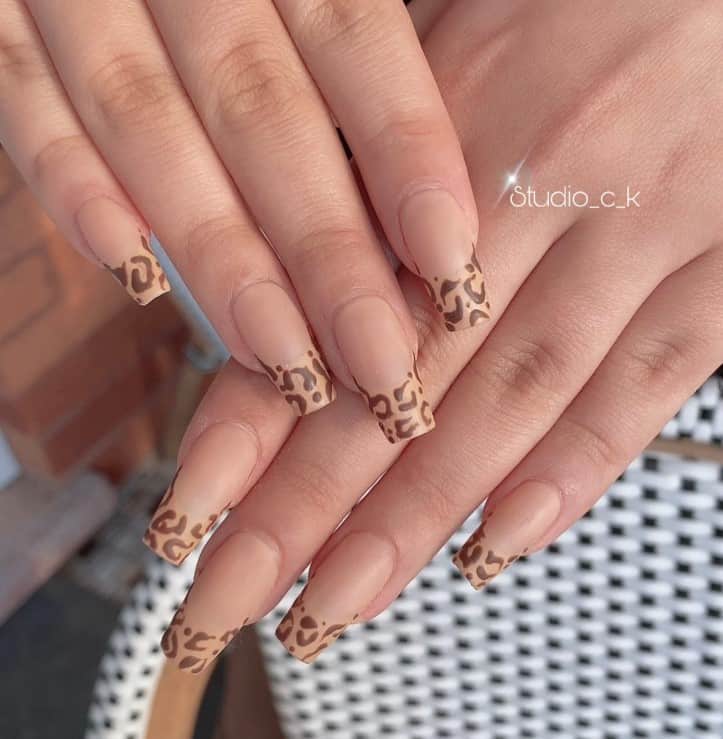 A woman's fingernails with nude nail polish that has leopard-print tips in different shades of brown
