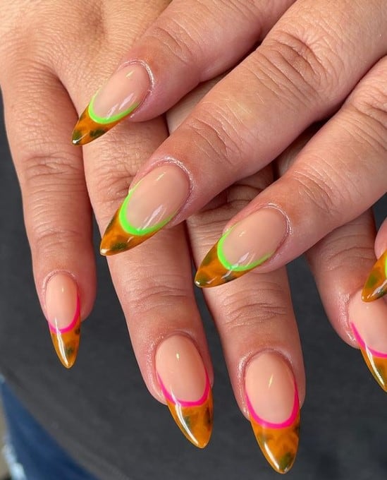 A closeup of a woman's fingernails with nude nail polish that has tortoiseshell-print tips outlined with pink and neon-green nail polish 