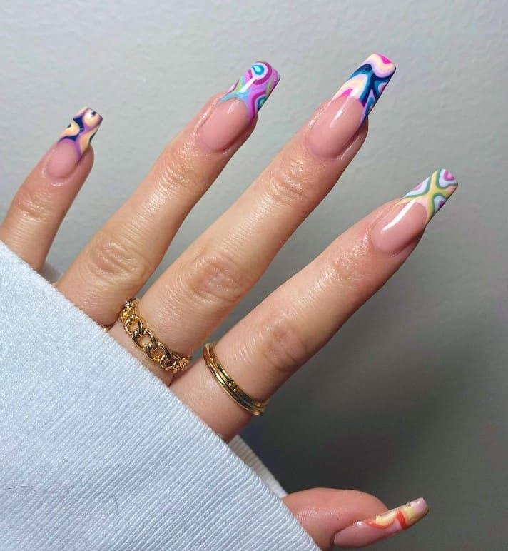 A woman's fingernails with pale pink nail polish that has swirly patterns with funky colors on each nail tips