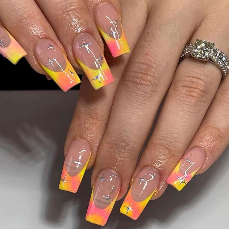 A closeup of a woman's finger with a glossy nude nail polish that has mix of yellow, orange, and pink on French tips