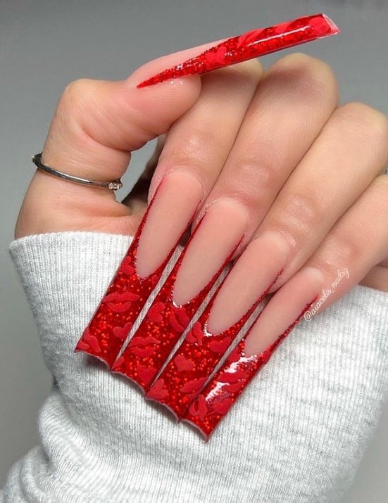 A closeup of a woman's long fingernails with a nude matte nail polish that has red lips and red hearts on nail tips 